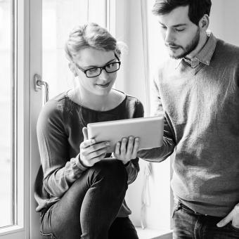 Two coworkers looking at a tablet standing near a window