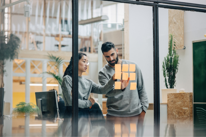 Two people looking at sticky notes on a glass wall