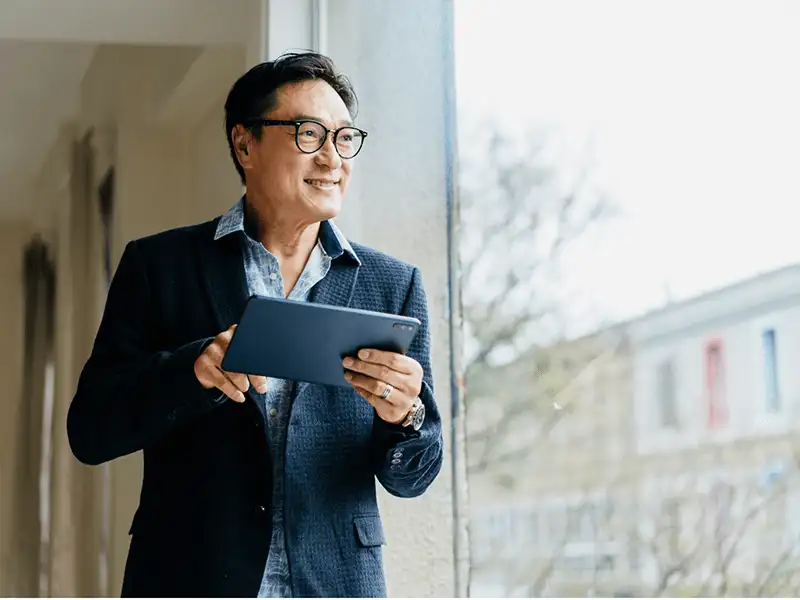 Hombre sonriente sostiene una tablet mientras mira por la ventana