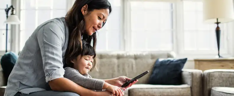 Woman holding her young child while looking at her phone in a living room setting