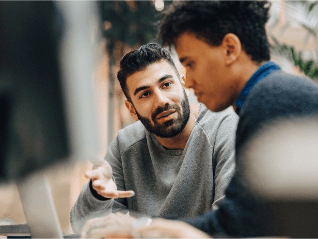 Duas pessoas colaborando à mesa com um laptop em segundo plano